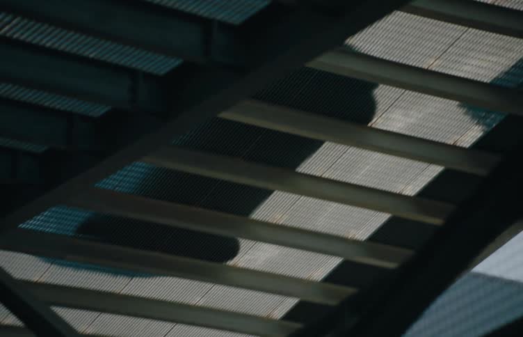 A blue car drives over a steel bridge at midday
