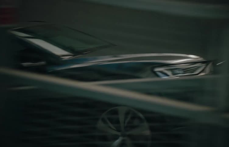 A dark modern suv with sleek lines drives quickly from left to right in a dimly lit industrial setting