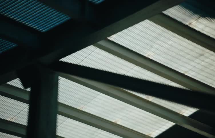 Steel beams and the underside of a car driving on a transparent ramp passes by overhead