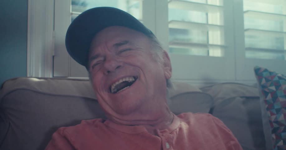 Elderly man is laughing while he watches television