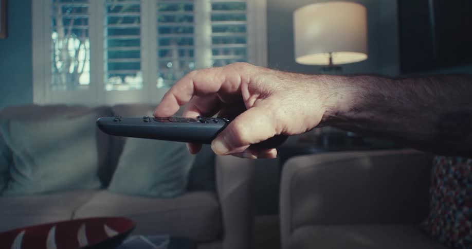 Close up of a mans hand as he operates an appliance in a living room with a remote control