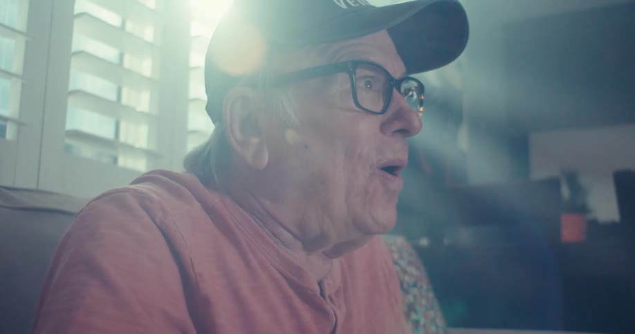 An elderly man is joyfully laughing in a warmly lit room slightly surprised