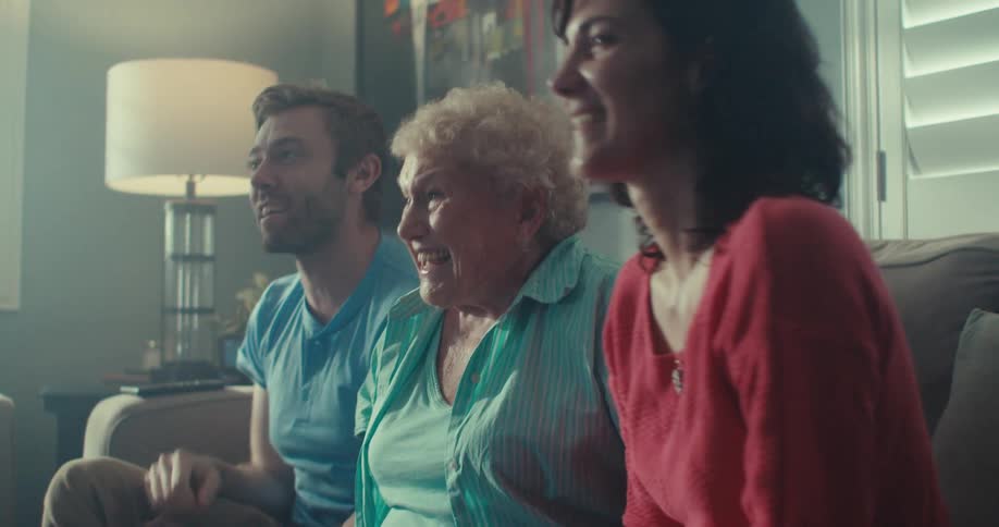 Three people are sitting on a sofa and are happy while looking forward in celebratory tones