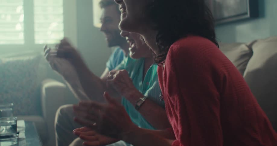 A family of three clap and celebrate while watching tv as they are seated in the living room