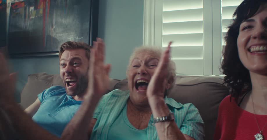 Three family members cheer excitedly while watching television together in a cozy living room