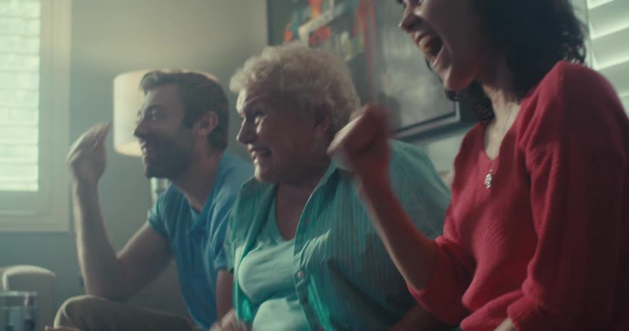 Three family members joyfully laugh together in a warmly lit living room