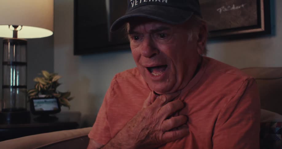 An elderly mansmiles joyfully while looking at a tablet indoors