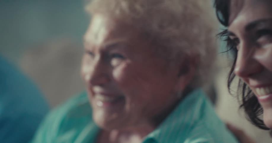 An elderly woman sits on a couch between two younger people all smiling and enjoying their time together