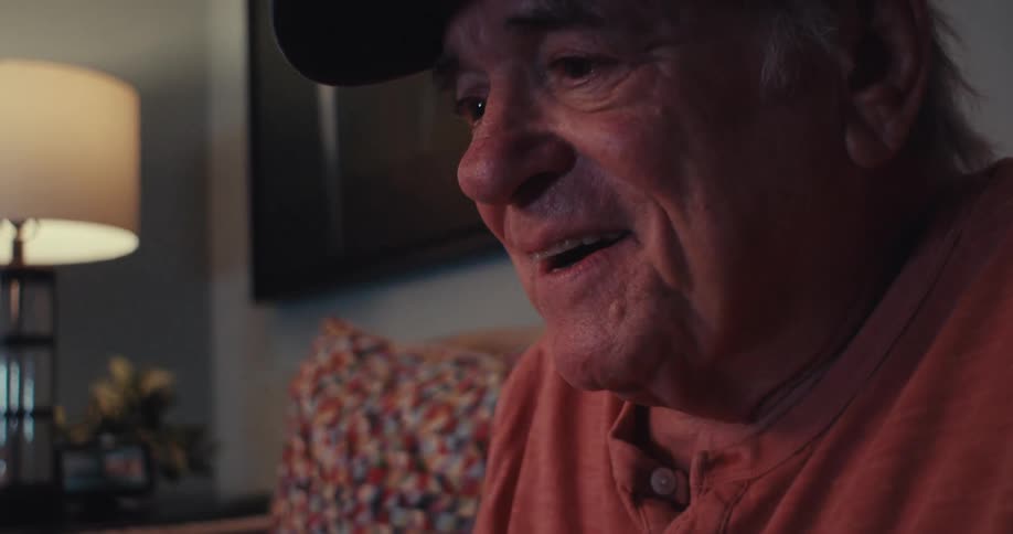 An elderly man smiles warmly during a video call in a cozy living room setting