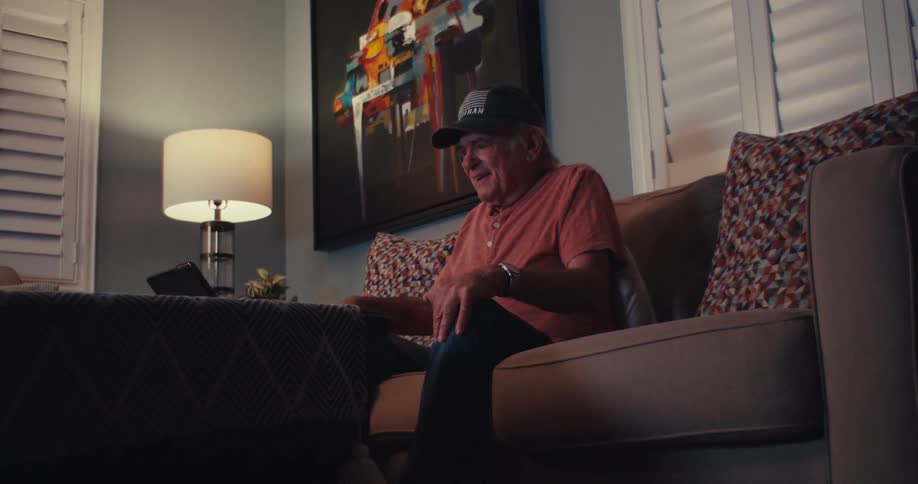 An elderly man celebrates joyfully while watching his tablet on the couch