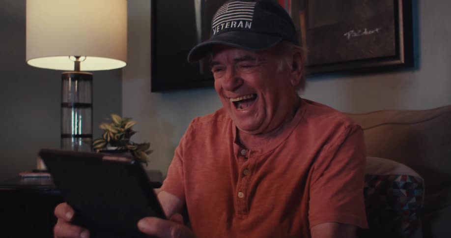 An elderly manjoyfully video chats on a tablet indoors