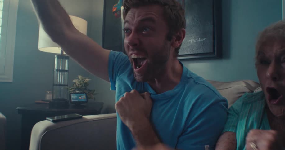 Man screams celebrates with his family as they watch tv while sitting in the living room