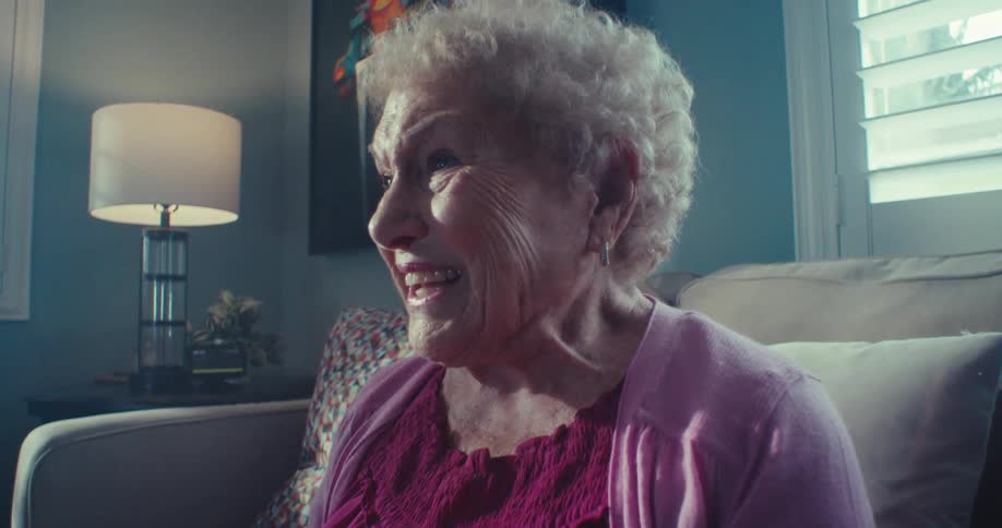 Elderly woman is smiling as she watches tv indoors