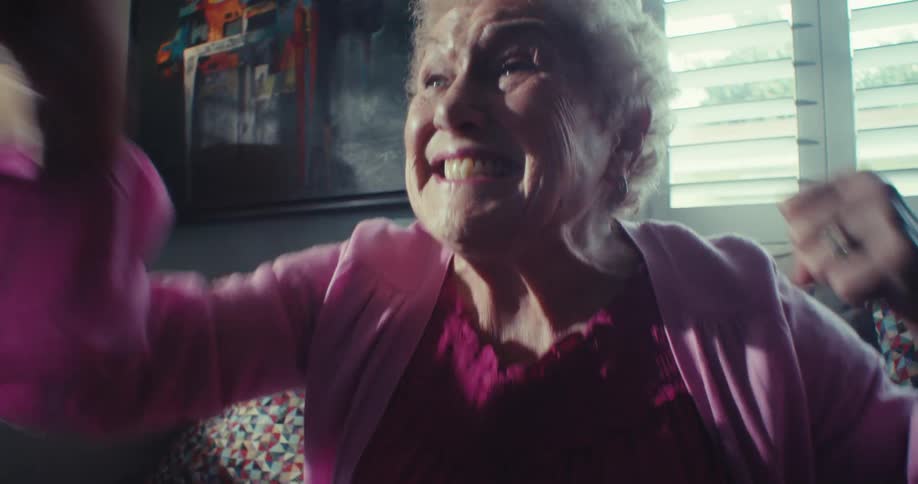 Elderly woman rejoices and celebrates while watching tv in a living room