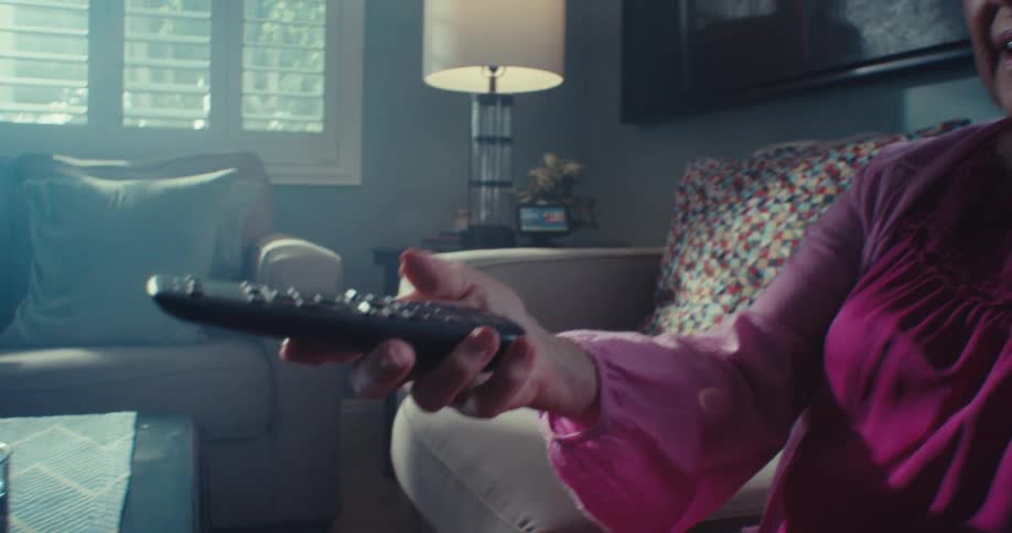 An elderly woman switches the channel on her television