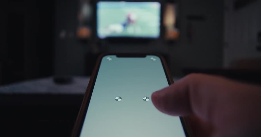 A person uses a smartphone as a remote control to play a game on a tv screen