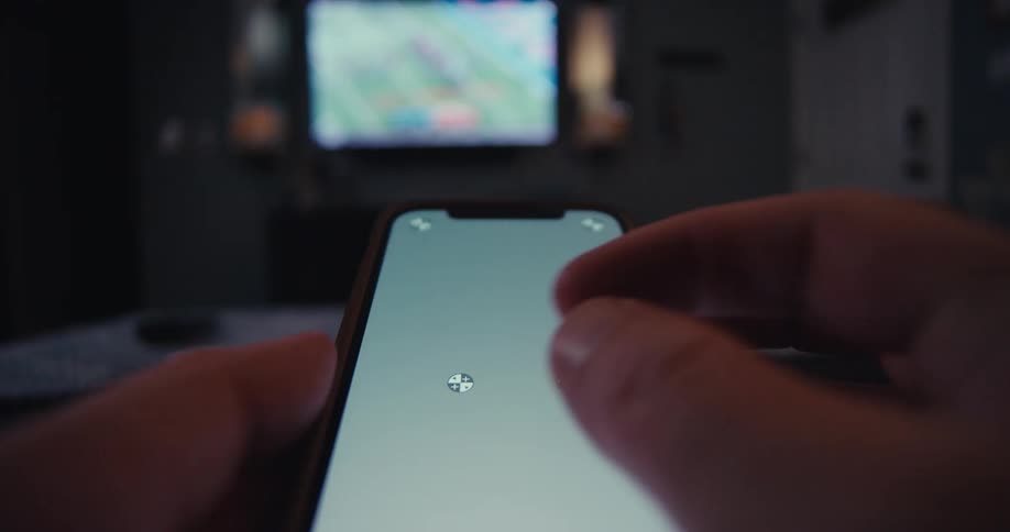 Person uses smartphone as remote while watching game in dim room