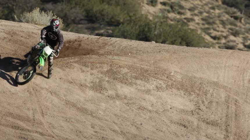 Person rides a dirt bike up and back down a dirt hill