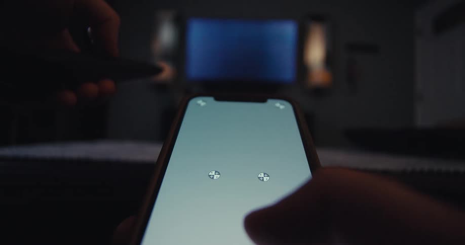 Person uses a smartphone to control a tv screen remotely in a dimly lit room