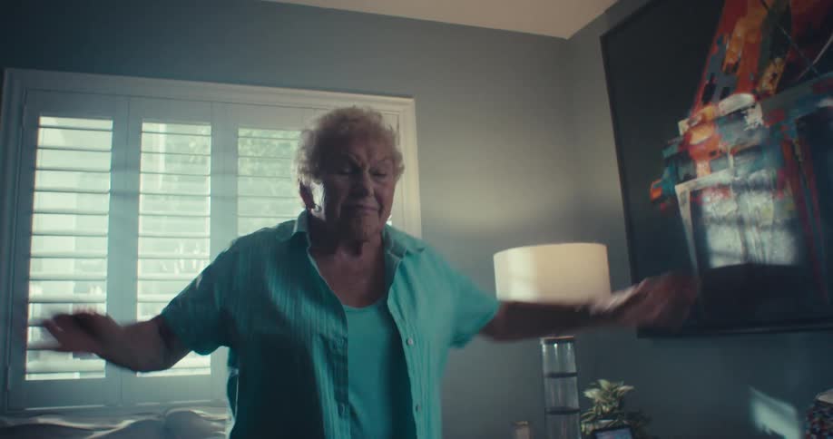 An elderly woman dances joyfully in a sunlit living room