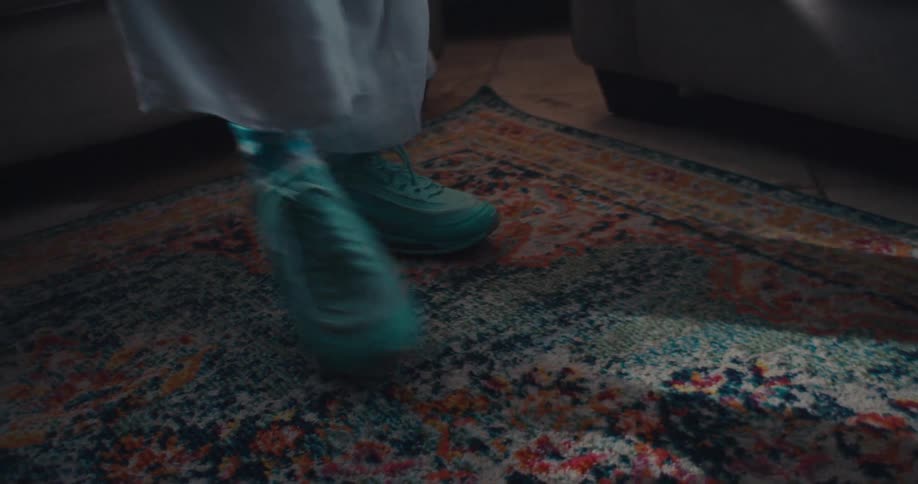 Closeup of a person dancing indoors wearing teal sneakers on a patterned rug