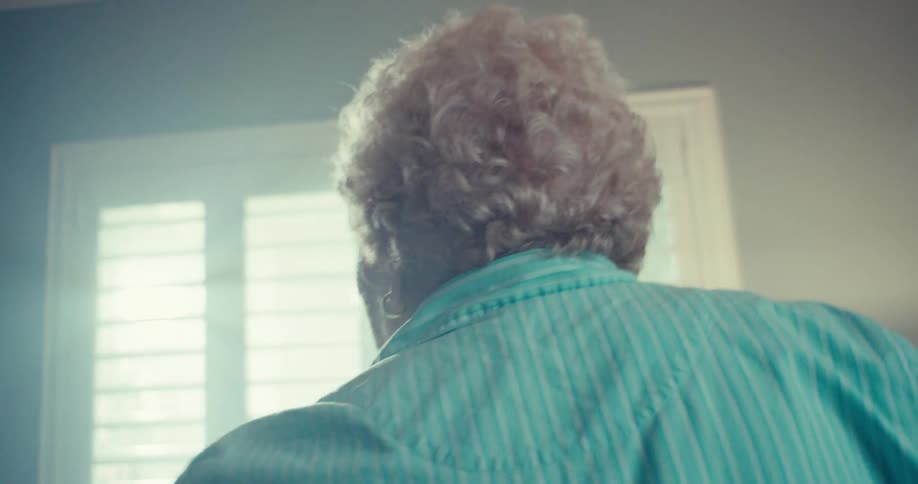 Elderly woman spins around with her arms out smiling as she dances in her living room