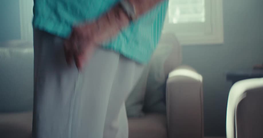 An elderly woman smiles joyfully while dancing indoors in a brightly lit room