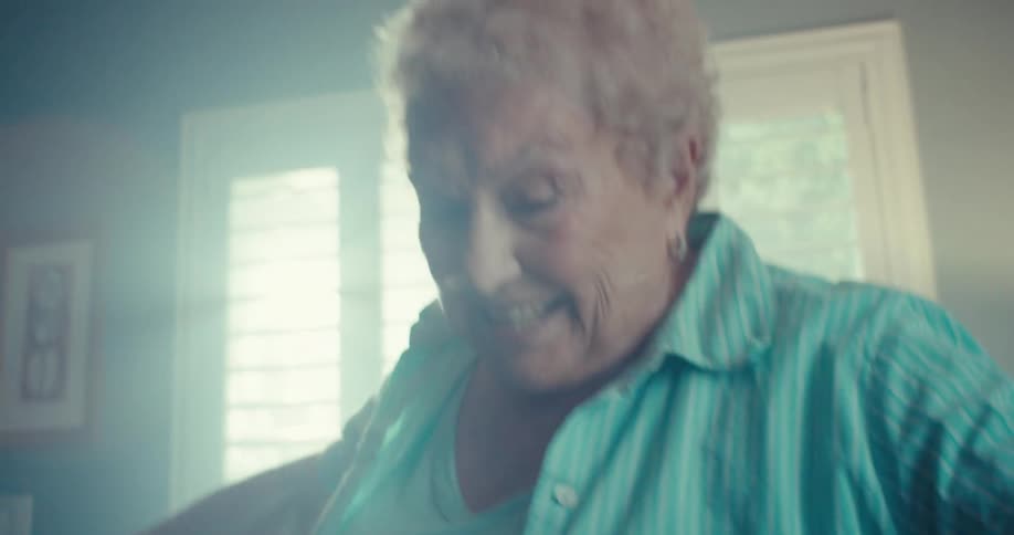A lady with short blonde hair is wearing blue sneakers doing some dance steps indoors and she is happy