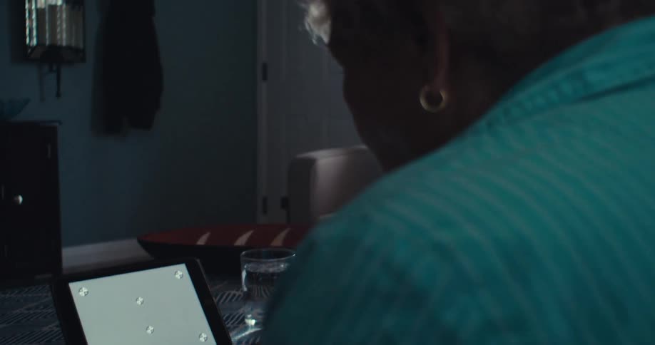 An elderly man is on a conference call using a tablet in his living room at midday