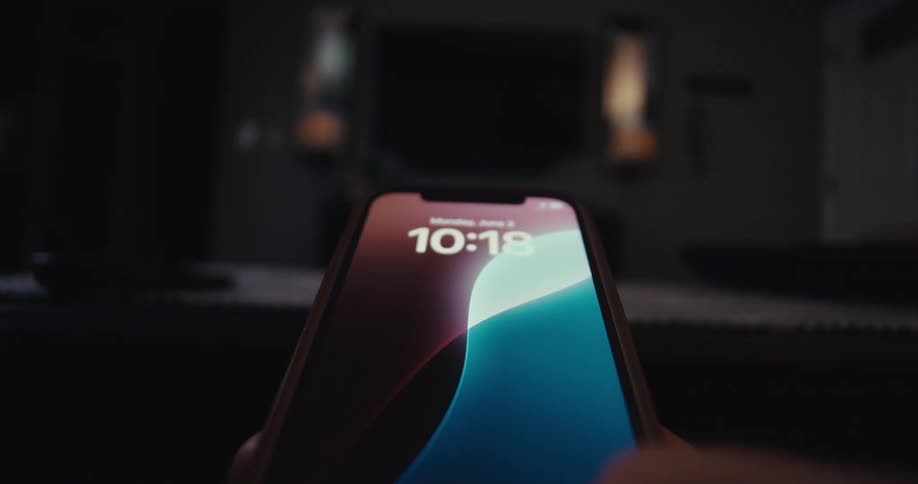 A person holds and scrolls through an iphone while using a remote to operate a tv