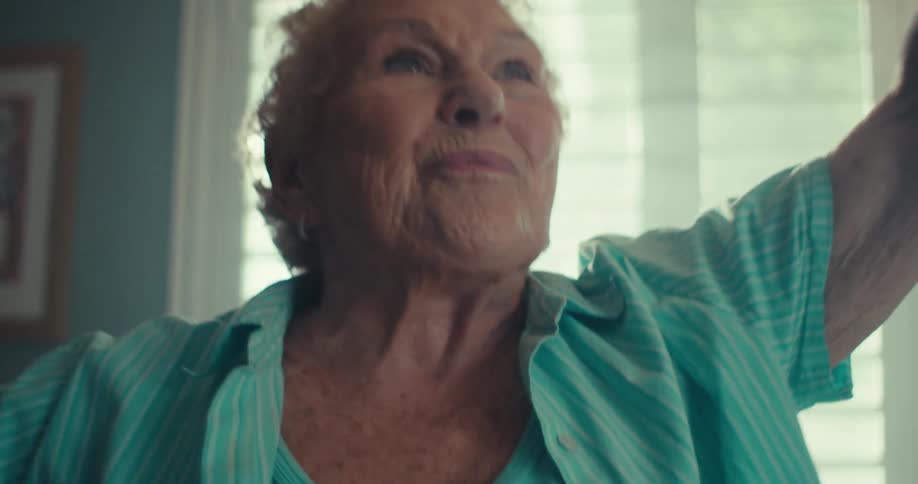 An elderly woman is dancing joyfully indoors with a warm expressive smile