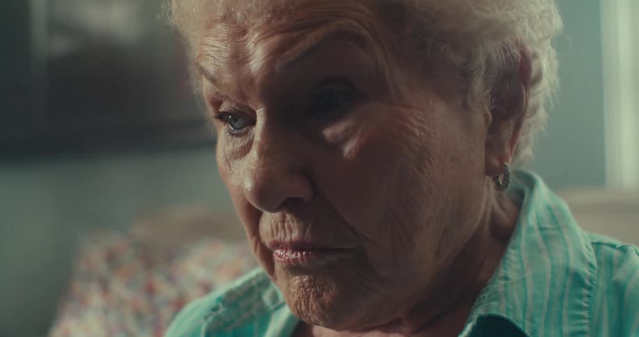 Elderly woman sitting at home leans forward and then back while focusing intently