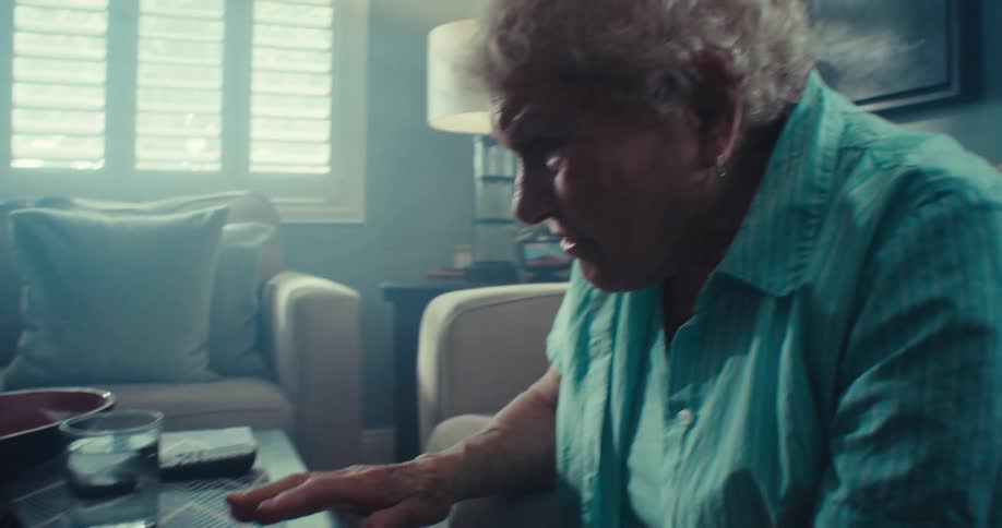 An elderly woman with a focused expression types on a laptop in her living room