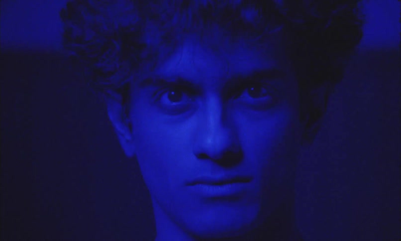 Young man stares intensely under moody blue lighting