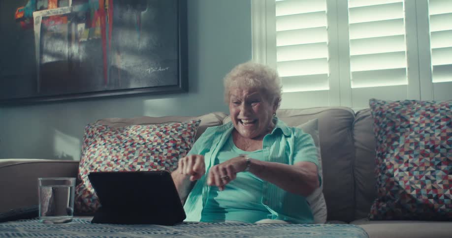 Elderly woman gestures and celebrates while on a video call with a tablet device in a living room