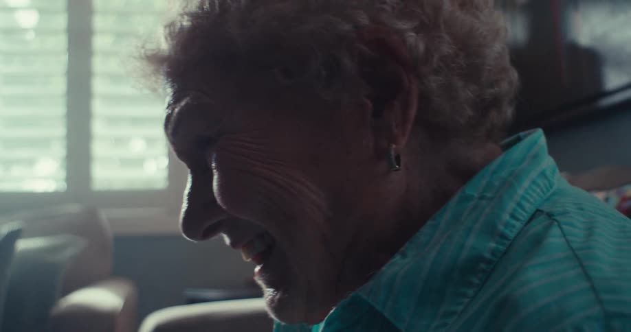 An elderly woman is smiling and laughing while sitting on a couch