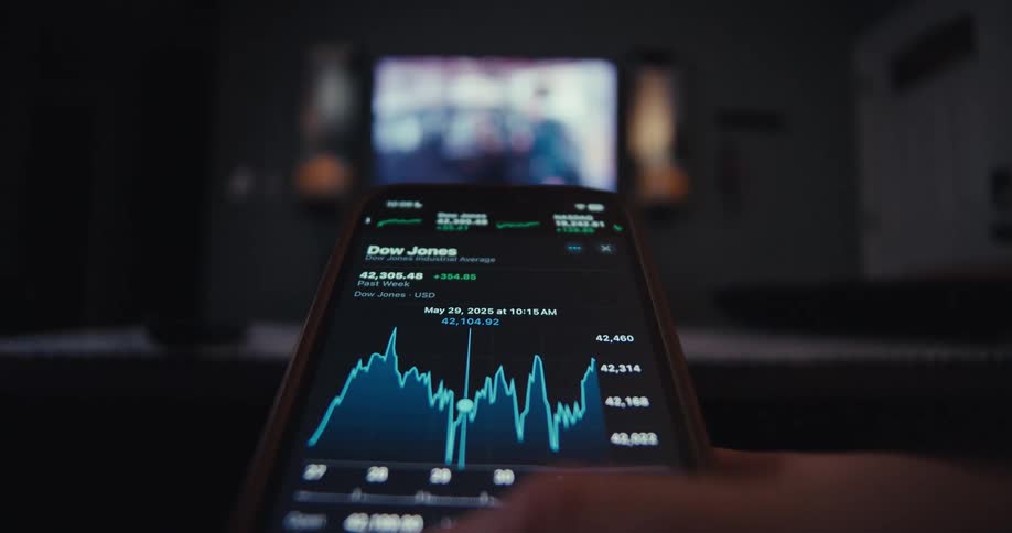 A smartphone shows a stock chart with a blurry tv in the background