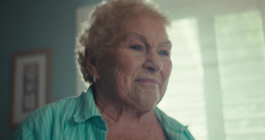 An elderly woman smiles joyfully while dancing in a warmly lit room