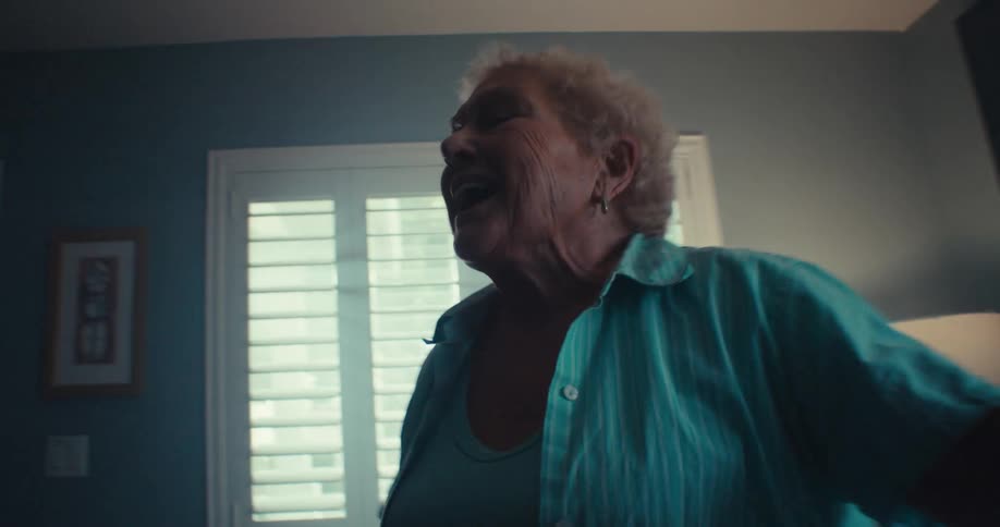 Elderly woman dances and sings happily while standing in a living room