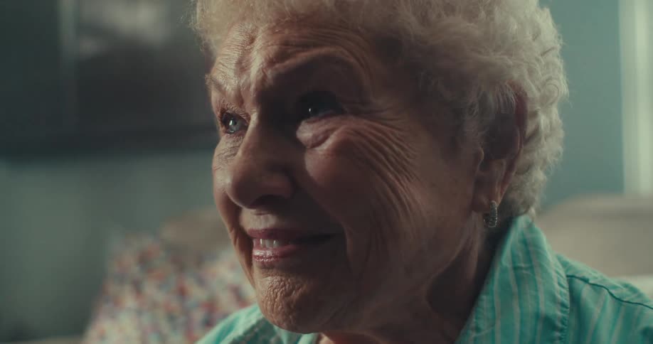An elderly woman smiles warmly in a softly lit indoor setting