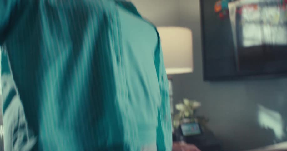 Elderly woman wearing turquois blue shoes socks and layered tops dances around waving her arms and shuffling her feet in her naturally sunlit living room during the day