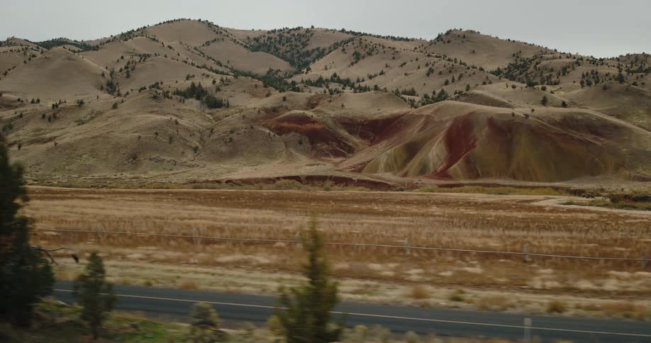 Painted hills and dry landscape with sparse trees in front of a mountainous backdrop