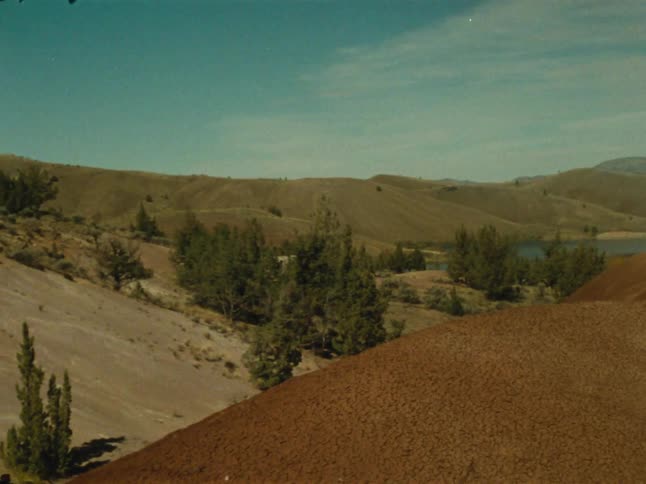 A vast arid landscape of rolling hills a winding river and distant mountains under a hazy sky