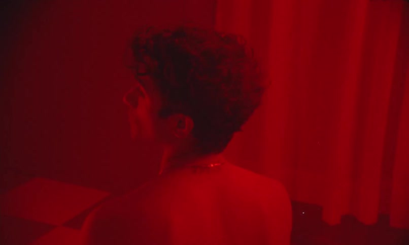 A person sits facing away under moody red lighting in a stylized indoor scene