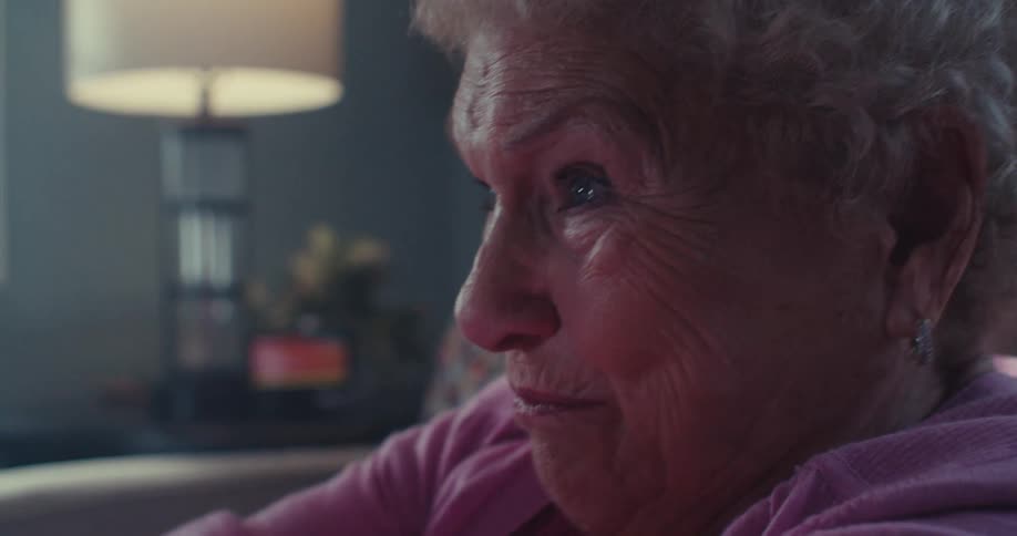 Elderly woman makes happy faces as she plays video games with a game controller in a living room