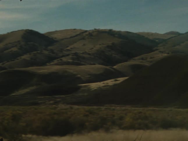 A vast dry landscape stretches beneath a cloudy sky with distant mountains on the horizon