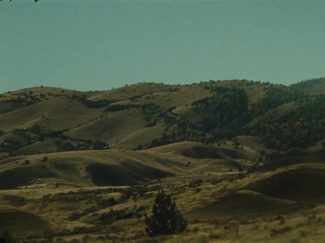 Rolling grassy hills under a partly cloudy sky in a mountainous landscape