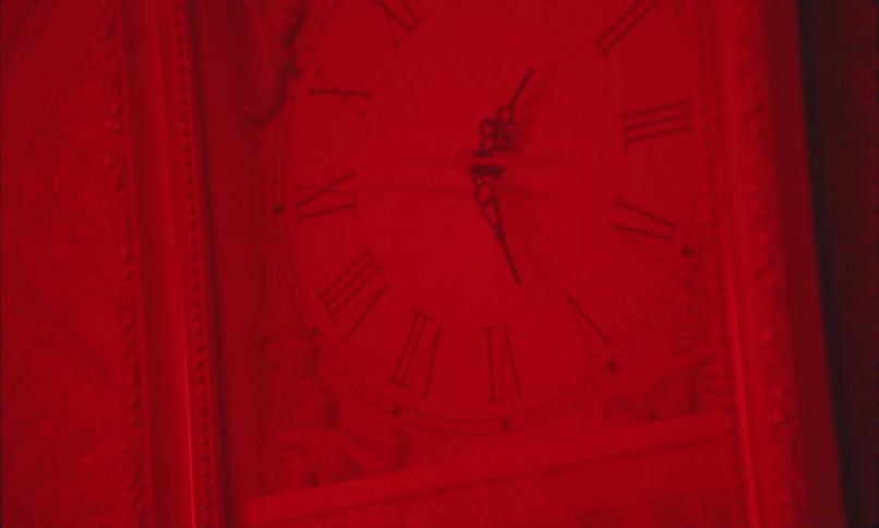 A clock face with roman numerals is illuminated with red light