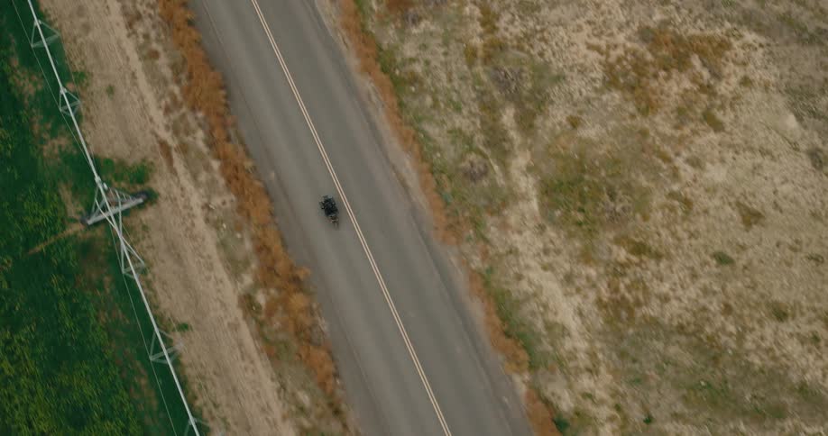 A motorcyclist rides along a rural highway near farmland