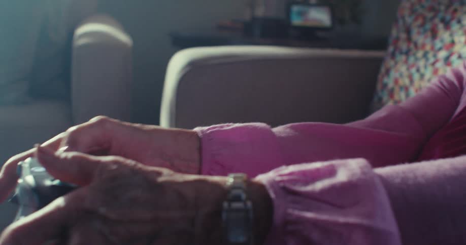 Elderly woman is playing video games and sitting on her couch